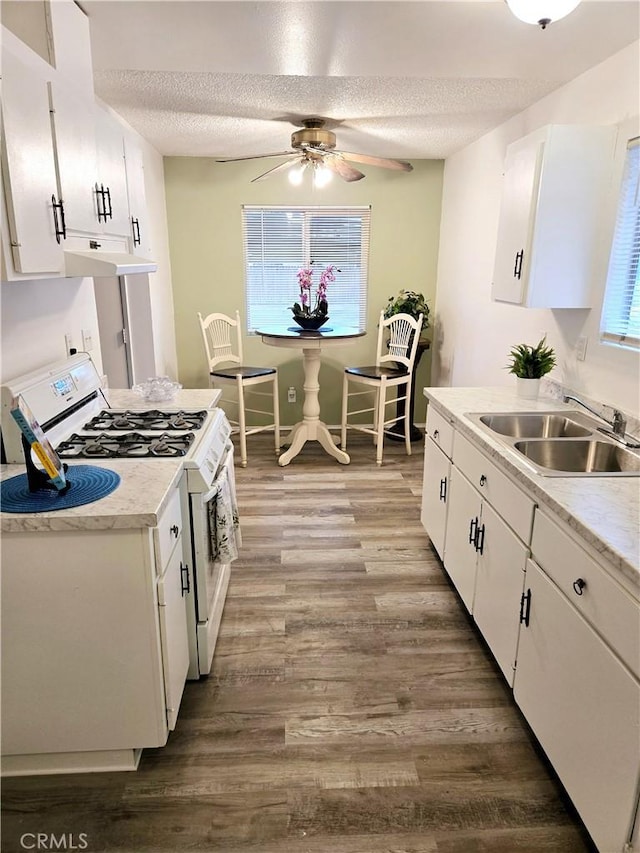 kitchen featuring a ceiling fan, white range with gas cooktop, a sink, under cabinet range hood, and a textured ceiling