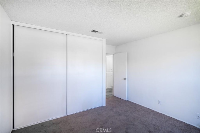 unfurnished bedroom with a closet, visible vents, carpet floors, and a textured ceiling