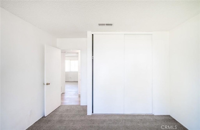 unfurnished bedroom featuring a closet, carpet flooring, a textured ceiling, and visible vents