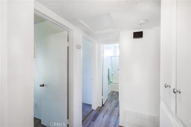 hallway featuring visible vents, a textured ceiling, and wood finished floors