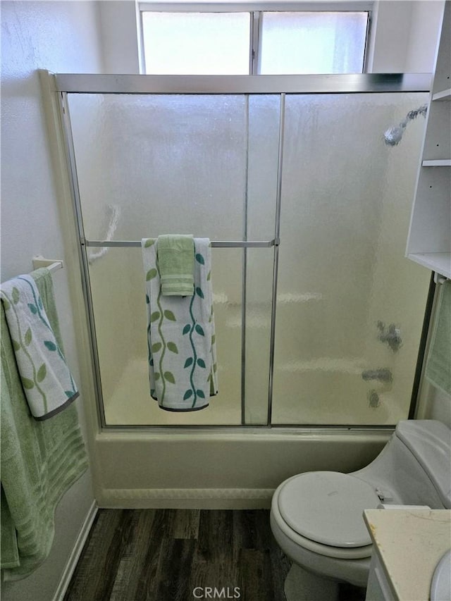 bathroom with vanity, toilet, wood finished floors, and bath / shower combo with glass door