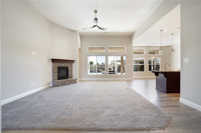 unfurnished living room with baseboards, a fireplace, a high ceiling, wood finished floors, and a ceiling fan