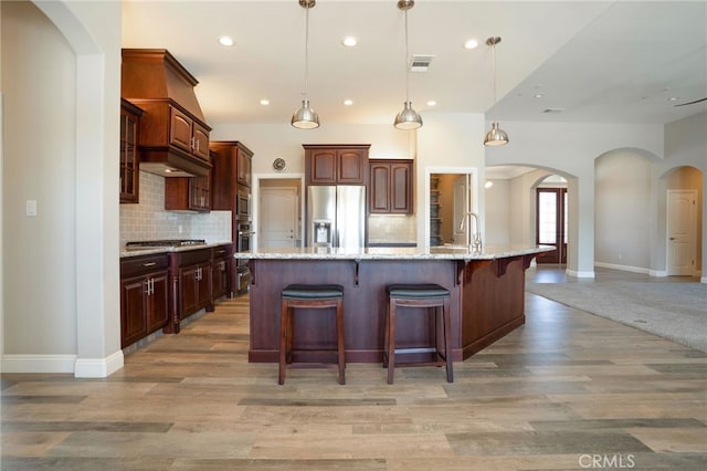 kitchen with visible vents, a kitchen bar, arched walkways, light wood-style floors, and appliances with stainless steel finishes