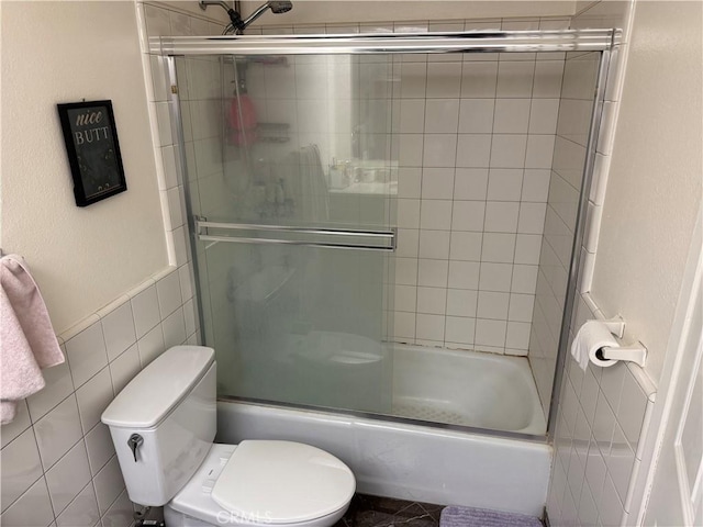 full bathroom featuring combined bath / shower with glass door, toilet, and tile walls