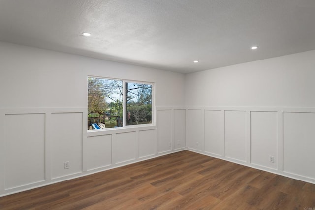 spare room with a textured ceiling, wood finished floors, recessed lighting, wainscoting, and a decorative wall