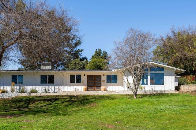 view of front facade with french doors, board and batten siding, and a front lawn