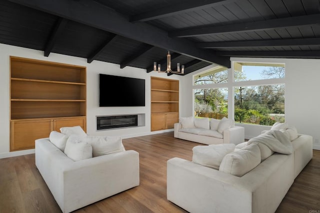 living area with lofted ceiling with beams, a glass covered fireplace, a chandelier, wood finished floors, and wood ceiling