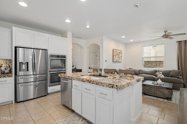 kitchen featuring a sink, arched walkways, appliances with stainless steel finishes, white cabinets, and light stone countertops