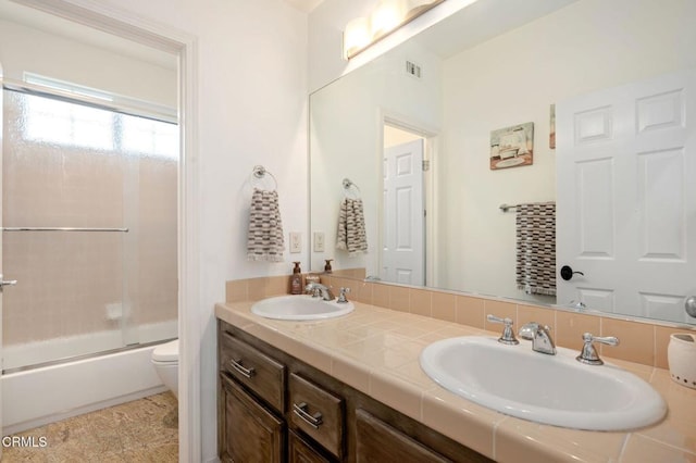 bathroom featuring a sink, enclosed tub / shower combo, toilet, and double vanity