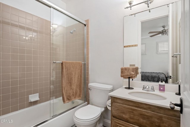 ensuite bathroom with connected bathroom, toilet, combined bath / shower with glass door, vanity, and a ceiling fan