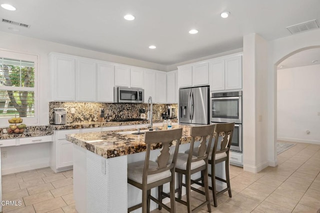 kitchen with visible vents, decorative backsplash, arched walkways, stainless steel appliances, and a sink