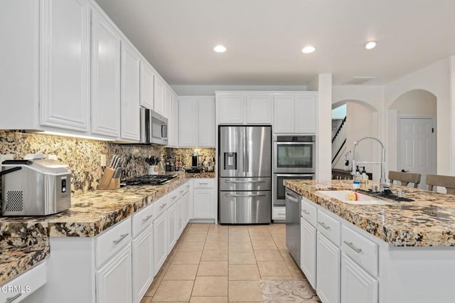 kitchen featuring white cabinets, arched walkways, appliances with stainless steel finishes, and a sink