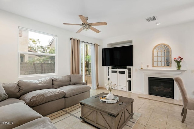 living area with light tile patterned floors, visible vents, a glass covered fireplace, and ceiling fan