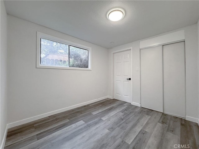 unfurnished bedroom with wood finished floors, baseboards, a closet, and a textured ceiling