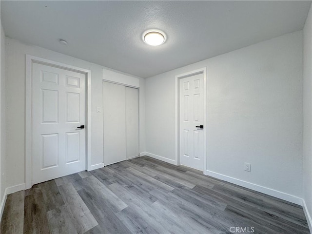 unfurnished bedroom featuring wood finished floors, baseboards, a closet, and a textured ceiling