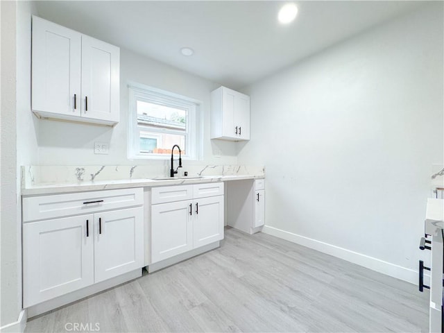 kitchen with white cabinets, light wood-style floors, baseboards, and a sink