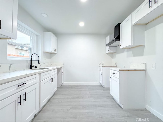 kitchen with light stone counters, baseboards, a sink, wall chimney exhaust hood, and light wood-type flooring