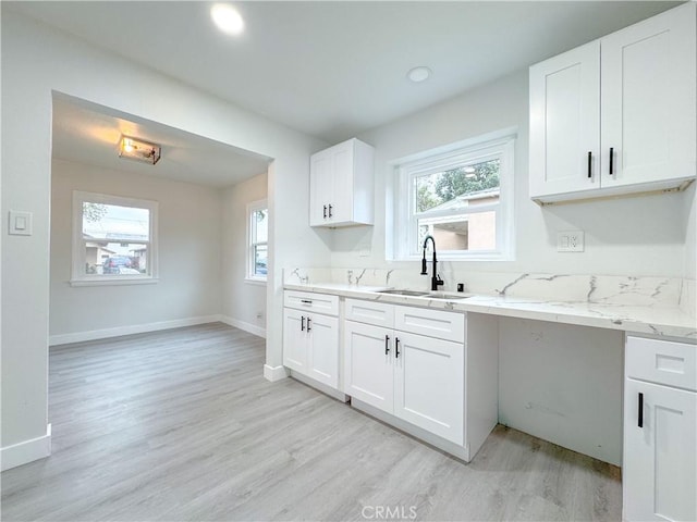 kitchen with light wood-style flooring, light stone counters, baseboards, and a sink