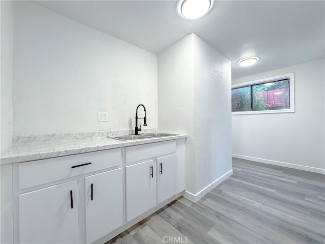 bar featuring light wood-type flooring, baseboards, and a sink