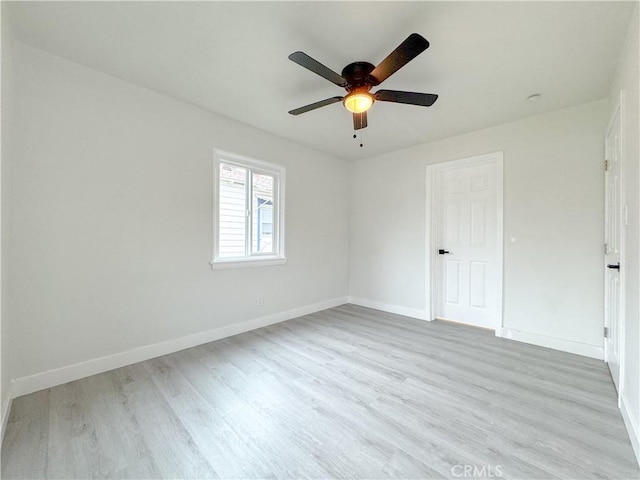 spare room with baseboards, light wood-style floors, and a ceiling fan