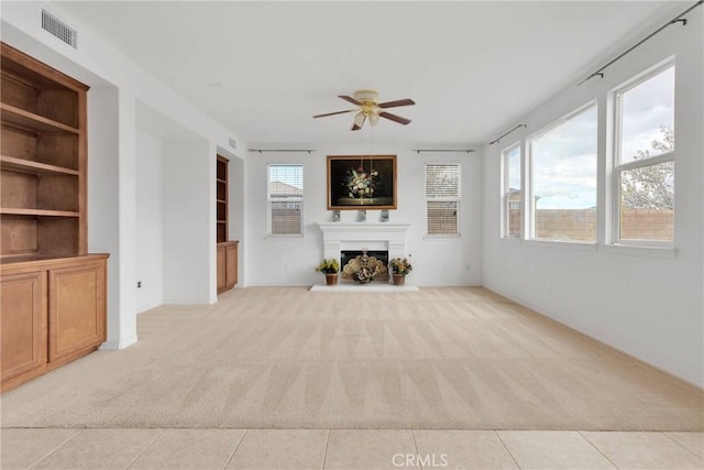 unfurnished living room with visible vents, light carpet, a healthy amount of sunlight, and a ceiling fan