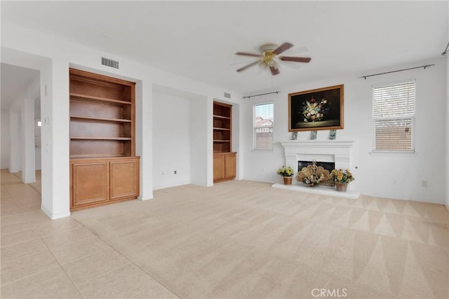 unfurnished living room featuring a healthy amount of sunlight, built in shelves, a ceiling fan, and light carpet