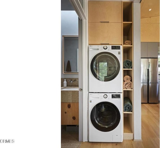 laundry room with laundry area, light wood-style flooring, a sink, and stacked washer and dryer