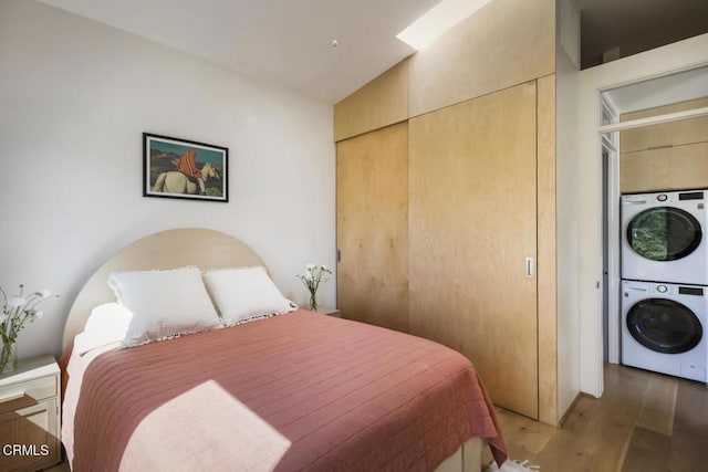 bedroom featuring a closet, stacked washer / dryer, and wood finished floors