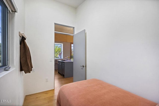 bedroom with light wood-type flooring, a high ceiling, and a sink