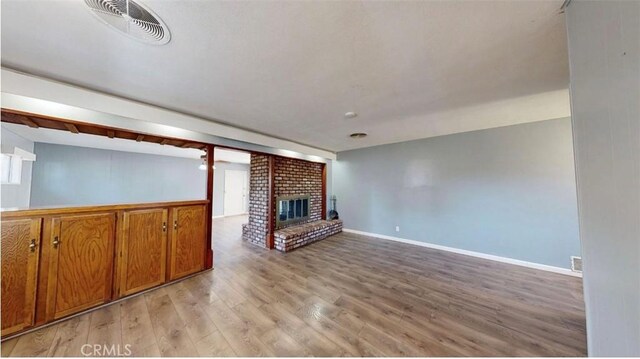unfurnished living room featuring light wood-type flooring, visible vents, baseboards, and a brick fireplace