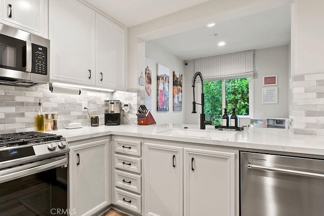 kitchen with light stone counters, a sink, white cabinets, appliances with stainless steel finishes, and tasteful backsplash