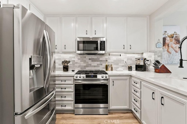 kitchen with light stone countertops, light wood finished floors, stainless steel appliances, decorative backsplash, and white cabinets