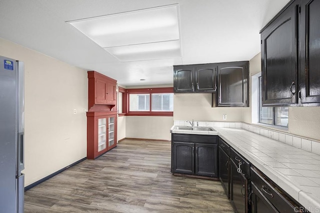 kitchen featuring baseboards, tile countertops, stainless steel refrigerator with ice dispenser, dark wood-style floors, and a sink