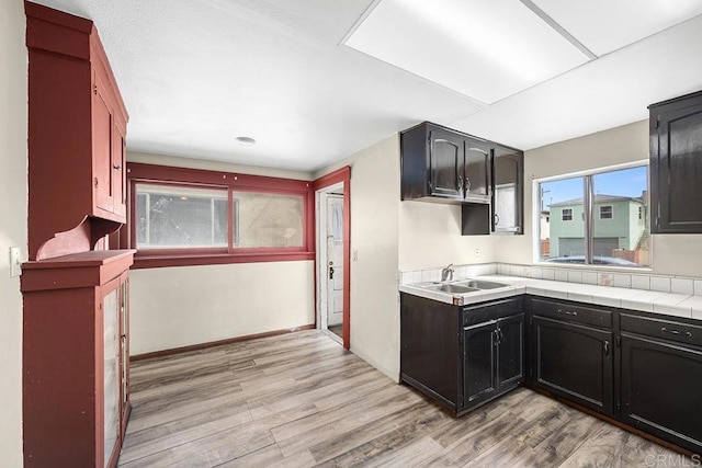 kitchen with baseboards, light wood finished floors, a sink, light countertops, and dark cabinets