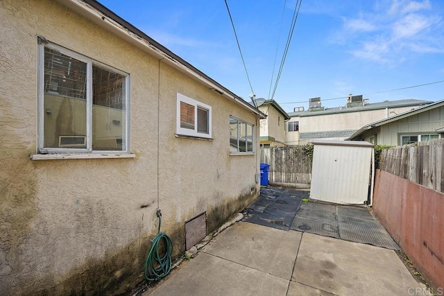 view of side of home with a patio, fence, an outbuilding, and stucco siding