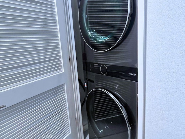 laundry room with laundry area, a textured wall, and stacked washer and clothes dryer