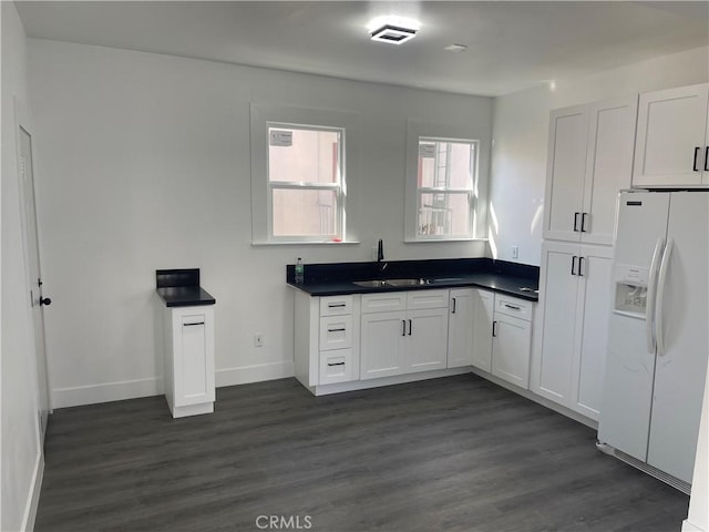 kitchen featuring dark countertops, dark wood-type flooring, white refrigerator with ice dispenser, white cabinetry, and a sink