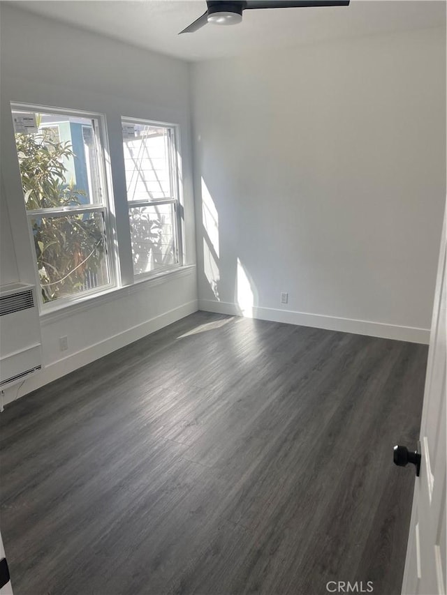 empty room with baseboards, ceiling fan, and dark wood-style flooring