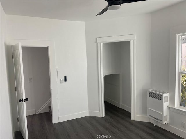 unfurnished bedroom featuring heating unit, ceiling fan, baseboards, and dark wood-style flooring