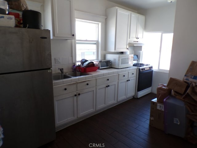 kitchen featuring range with gas stovetop, white microwave, dark wood-style flooring, freestanding refrigerator, and tile counters