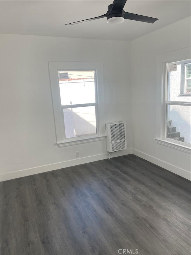 empty room featuring heating unit, baseboards, dark wood-style floors, and a ceiling fan