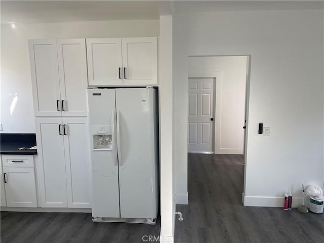 kitchen featuring dark countertops, dark wood finished floors, white cabinetry, white fridge with ice dispenser, and baseboards