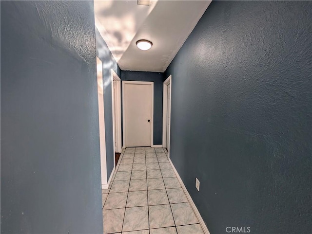 hall with light tile patterned floors, baseboards, and a textured wall