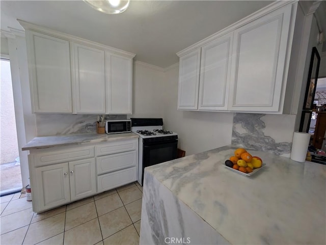 kitchen with light tile patterned floors, gas stove, ornamental molding, light countertops, and white cabinets