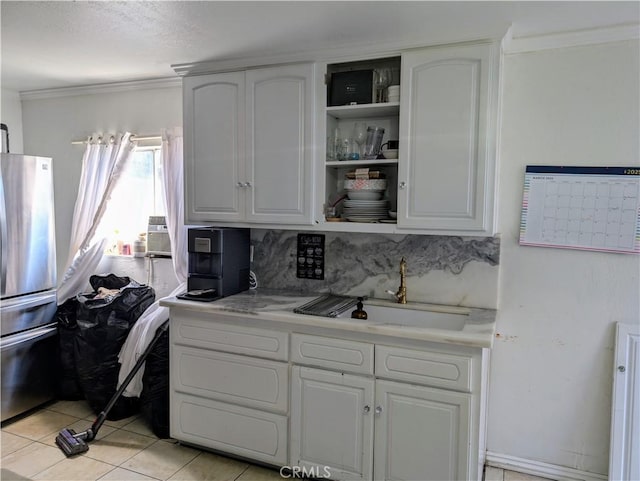 kitchen with a sink, freestanding refrigerator, white cabinets, crown molding, and light countertops