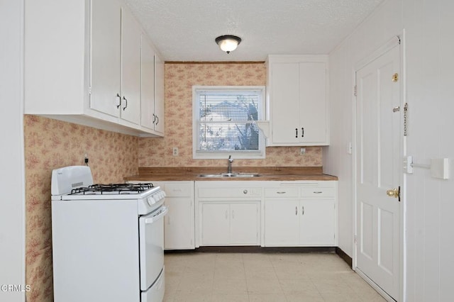 kitchen with white cabinetry, wallpapered walls, gas range gas stove, a textured ceiling, and a sink