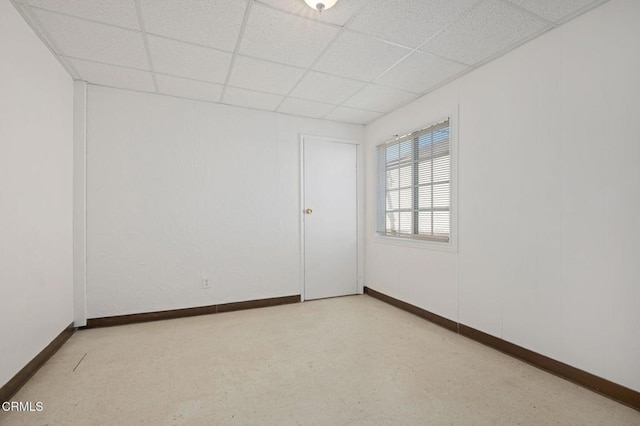 empty room featuring a paneled ceiling and baseboards