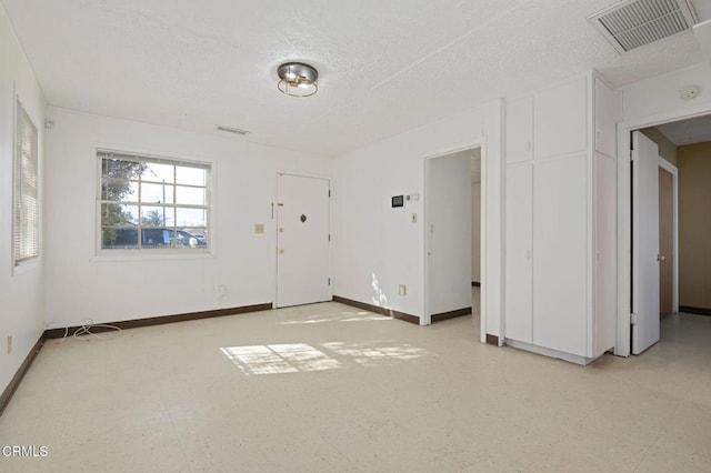 unfurnished room featuring visible vents, light floors, a textured ceiling, and baseboards