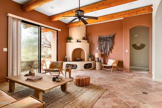 living area with beamed ceiling, a fireplace with raised hearth, arched walkways, baseboards, and ceiling fan