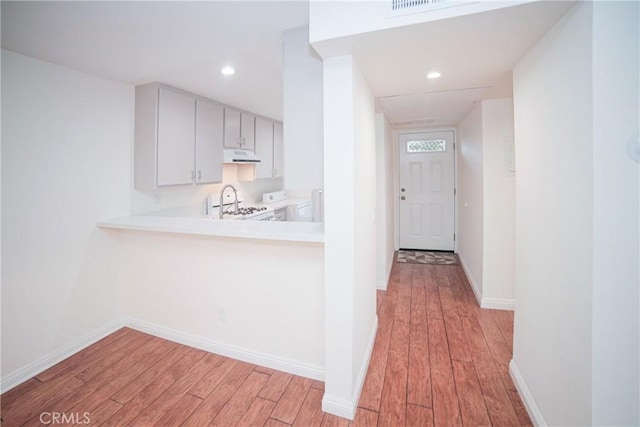 kitchen with light wood-style flooring, under cabinet range hood, light countertops, baseboards, and white gas range